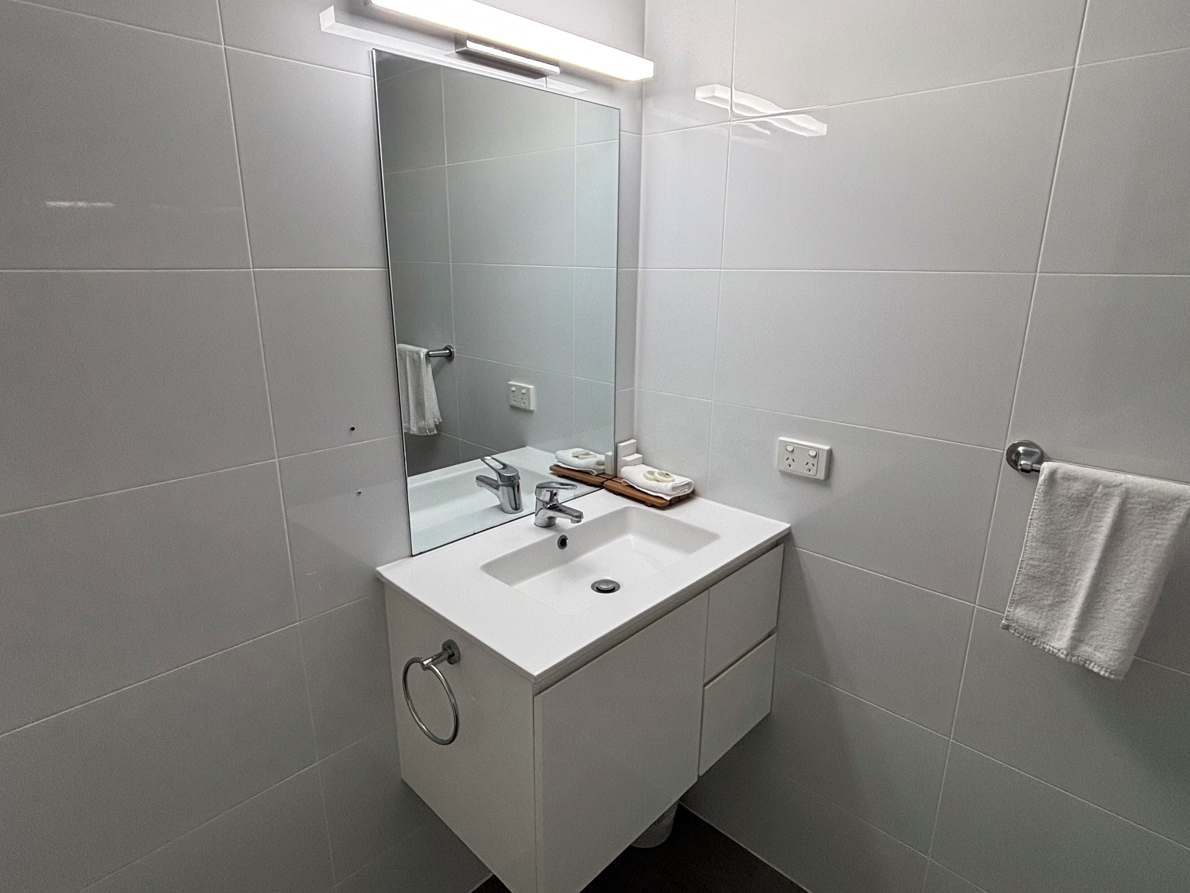 A modern bathroom with a white sink, mirror, and towel rack.