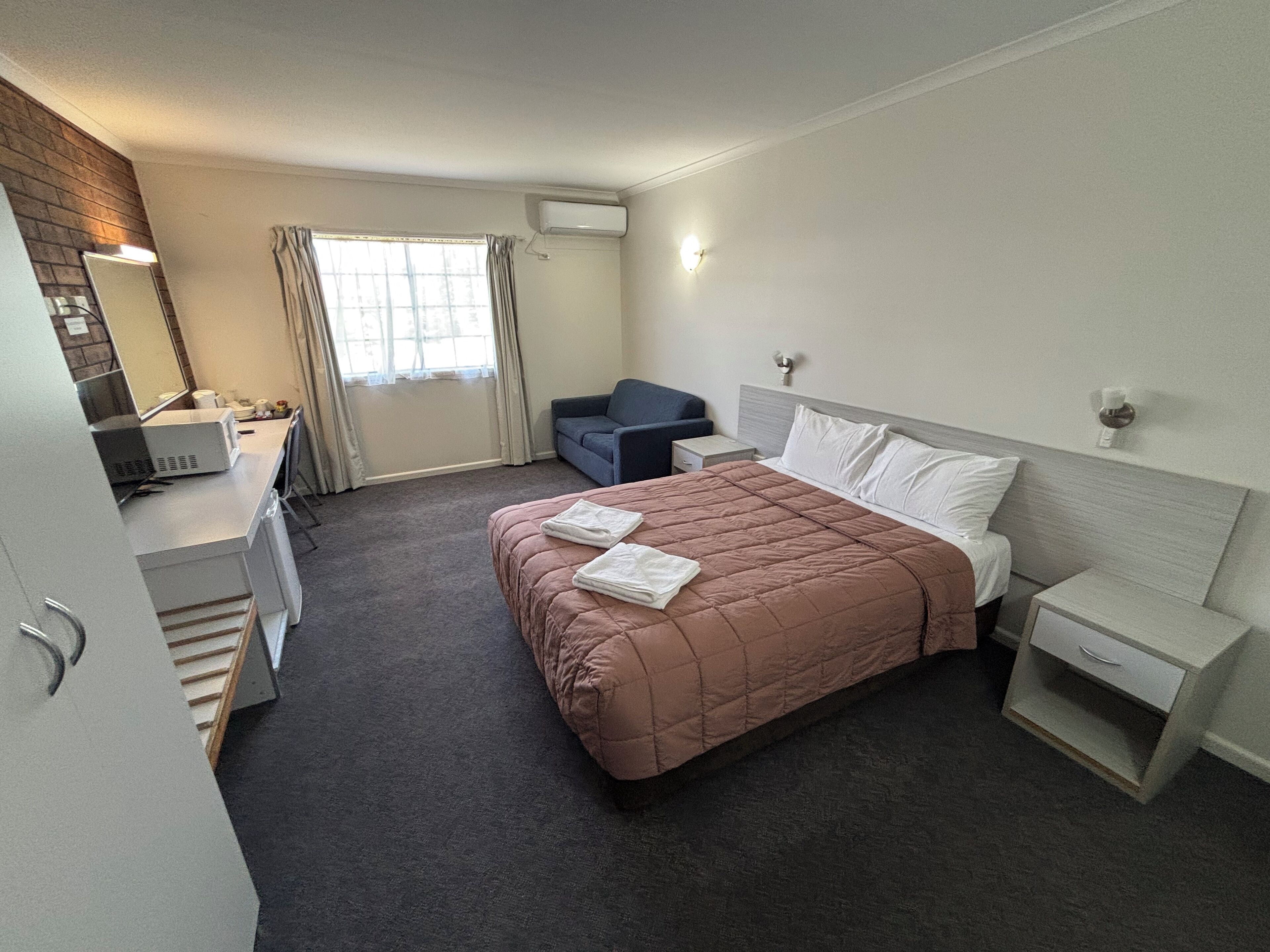 A hotel room with a bed, a desk, a chair, and a window.