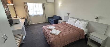 A hotel room with a bed, a desk, a chair, and a window.