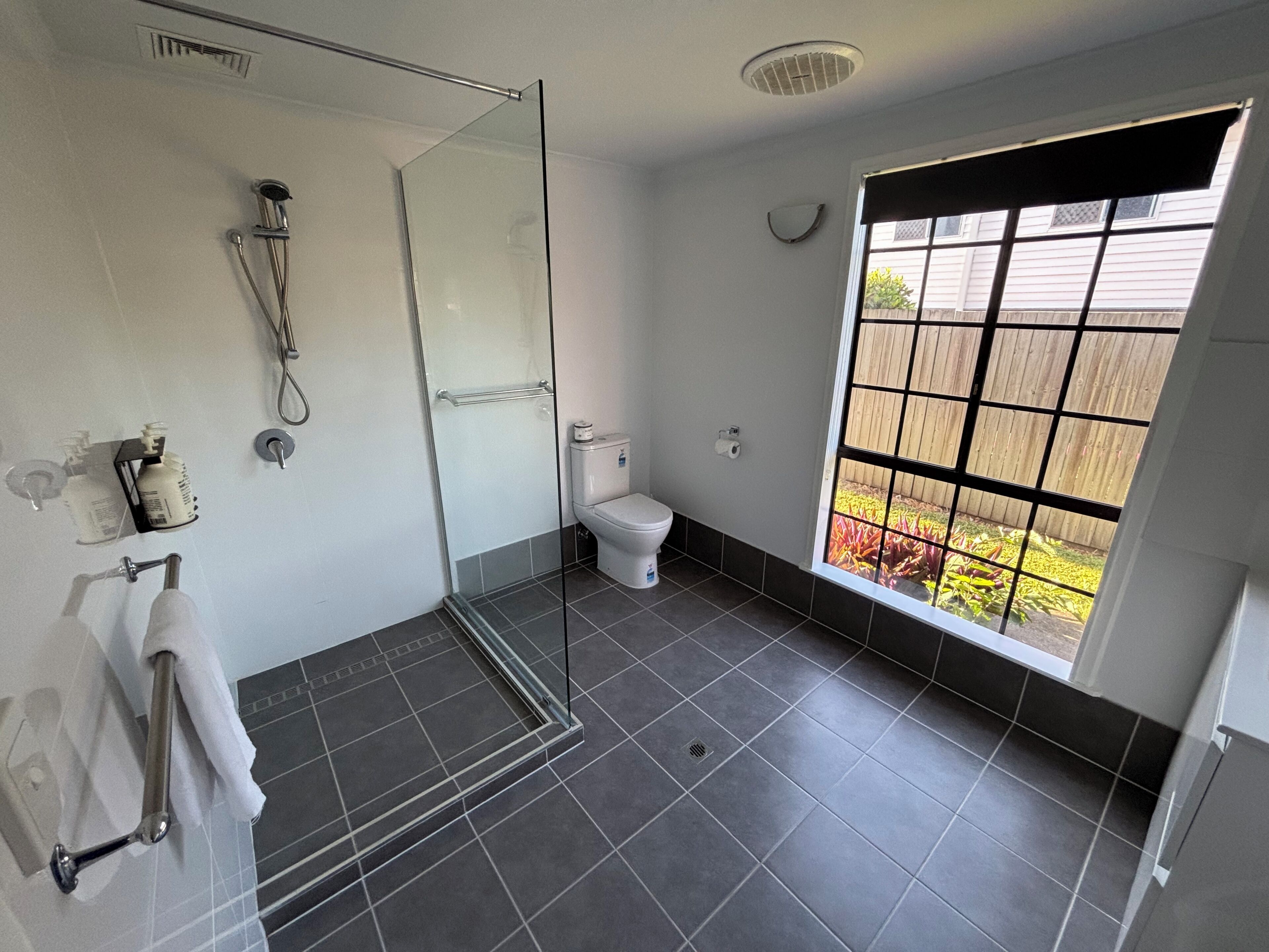 A modern bathroom with a glass shower enclosure, a toilet, and a window with a view of a garden.