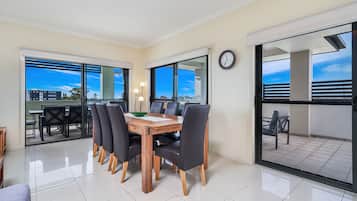 Comedor con mesa de madera y sillas negras, ventanas amplias y vistas a edificios y árboles.