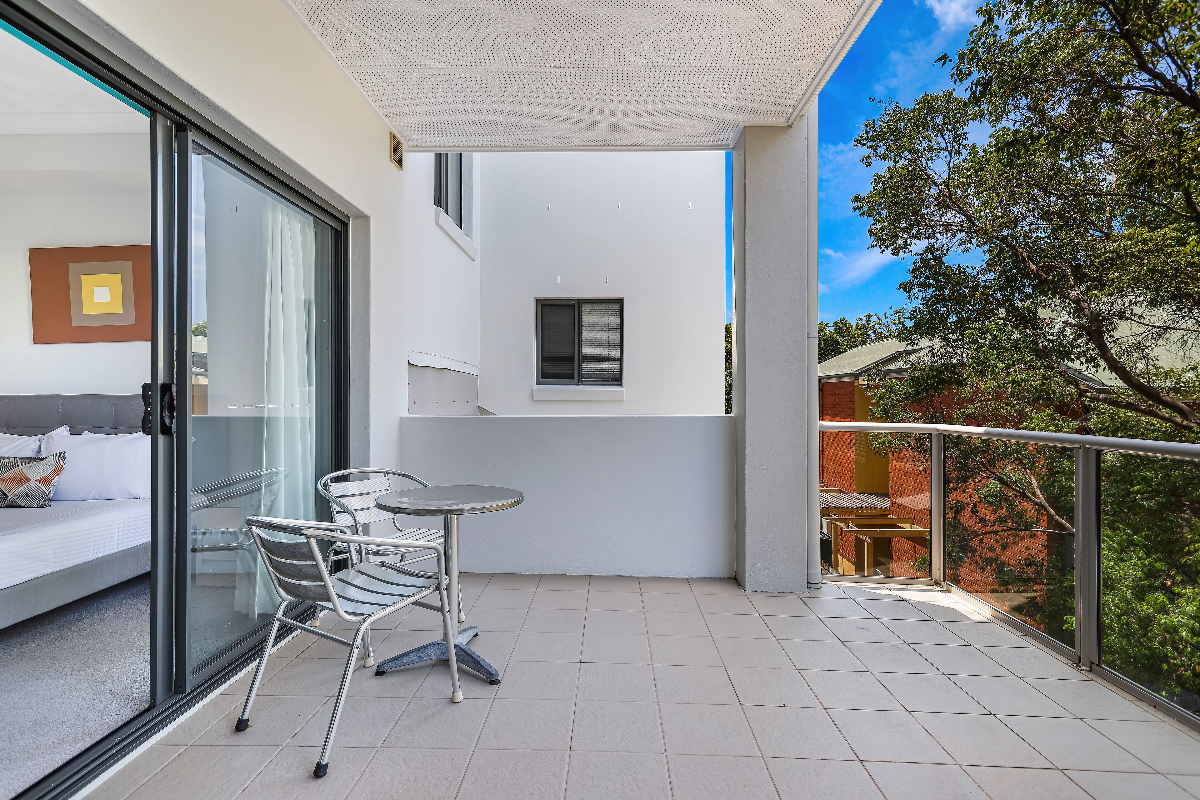 A balcony with a glass door, a bed, a small table, and chairs.
