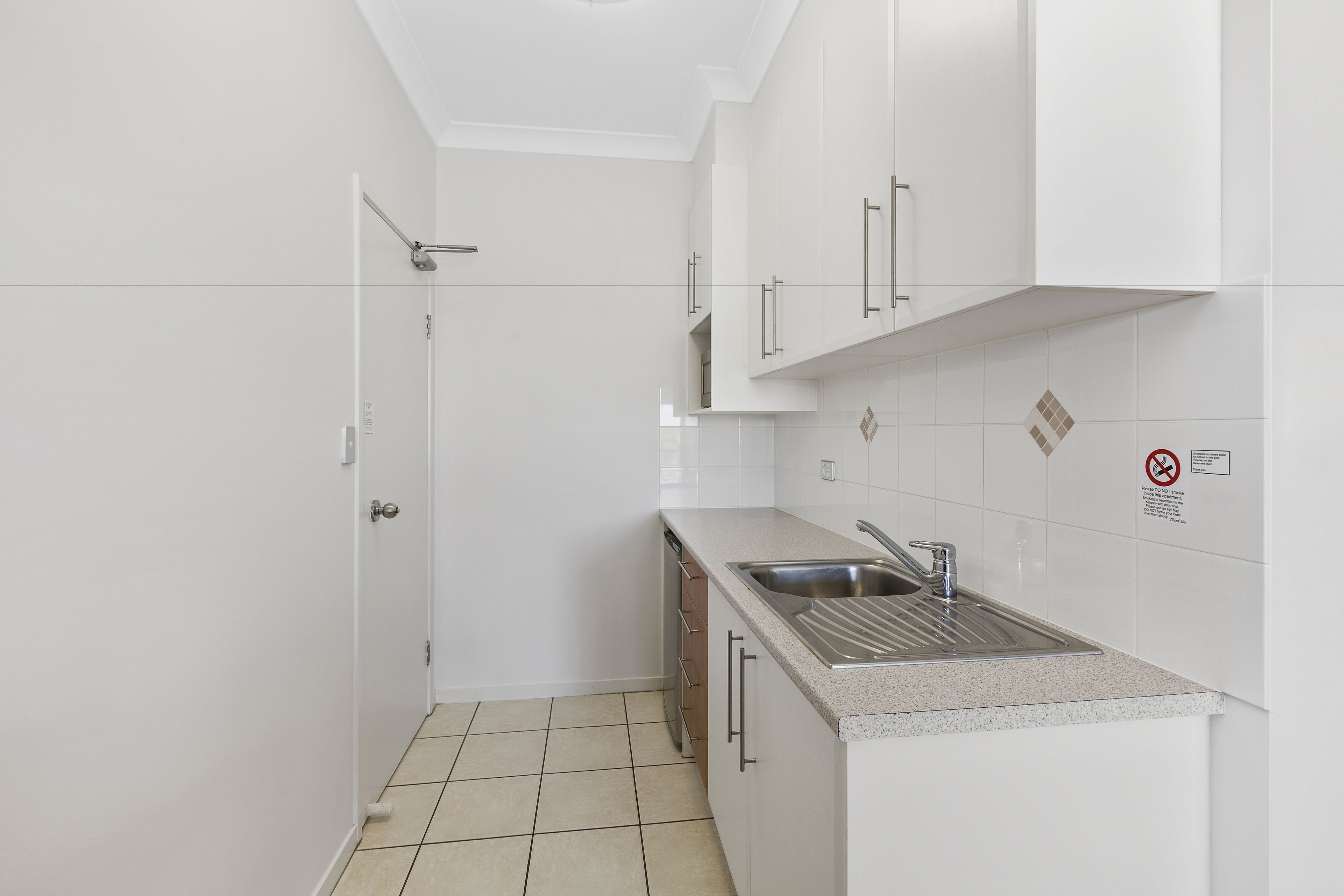 Eine kleine, moderne Küche mit weißen Schränken, einer Edelstahlspüle und einer gefliesten Spritzschutzwand.