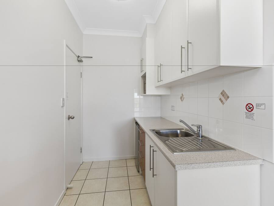 A small, modern kitchen with white cabinets, a stainless steel sink, and a tiled backsplash.