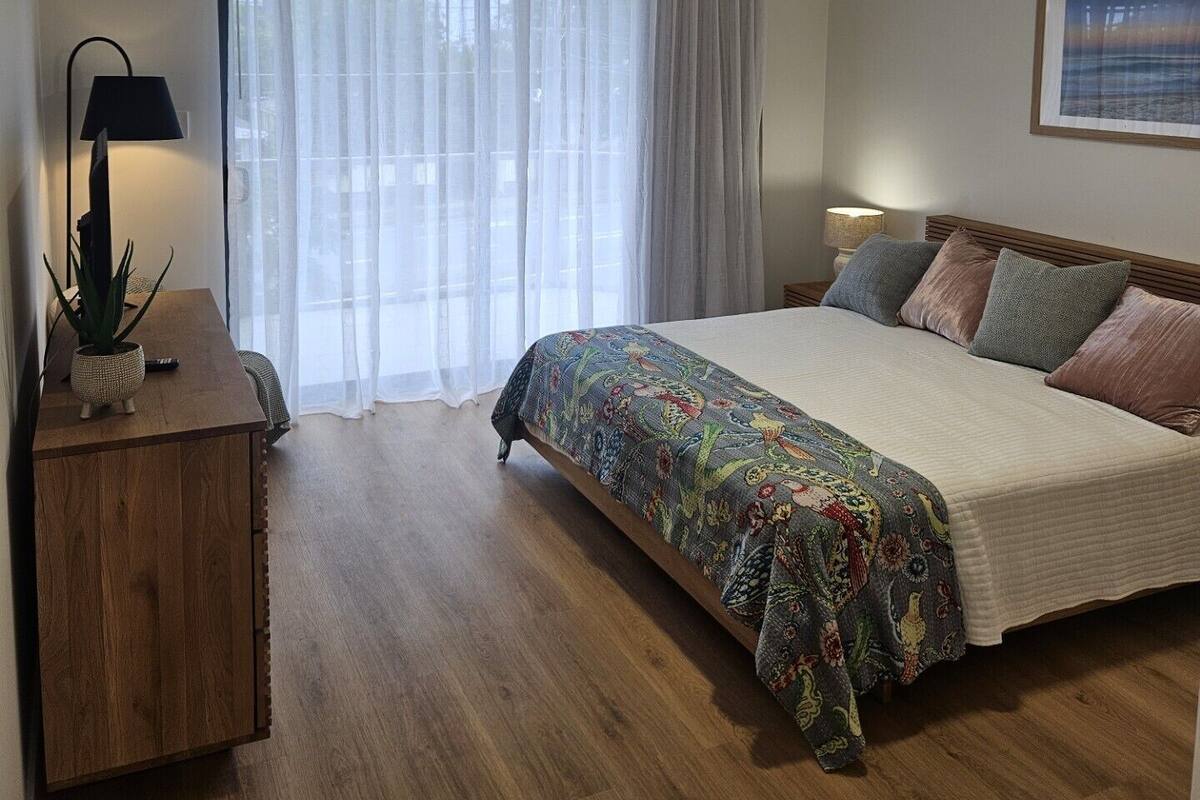 A bedroom with a bed, a desk with a lamp, a ceiling fan, and a window with curtains.