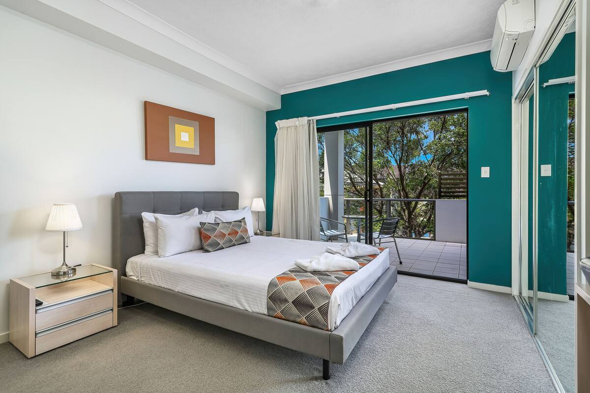 A modern bedroom with a bed, bedside table, and a view of the outside balcony.