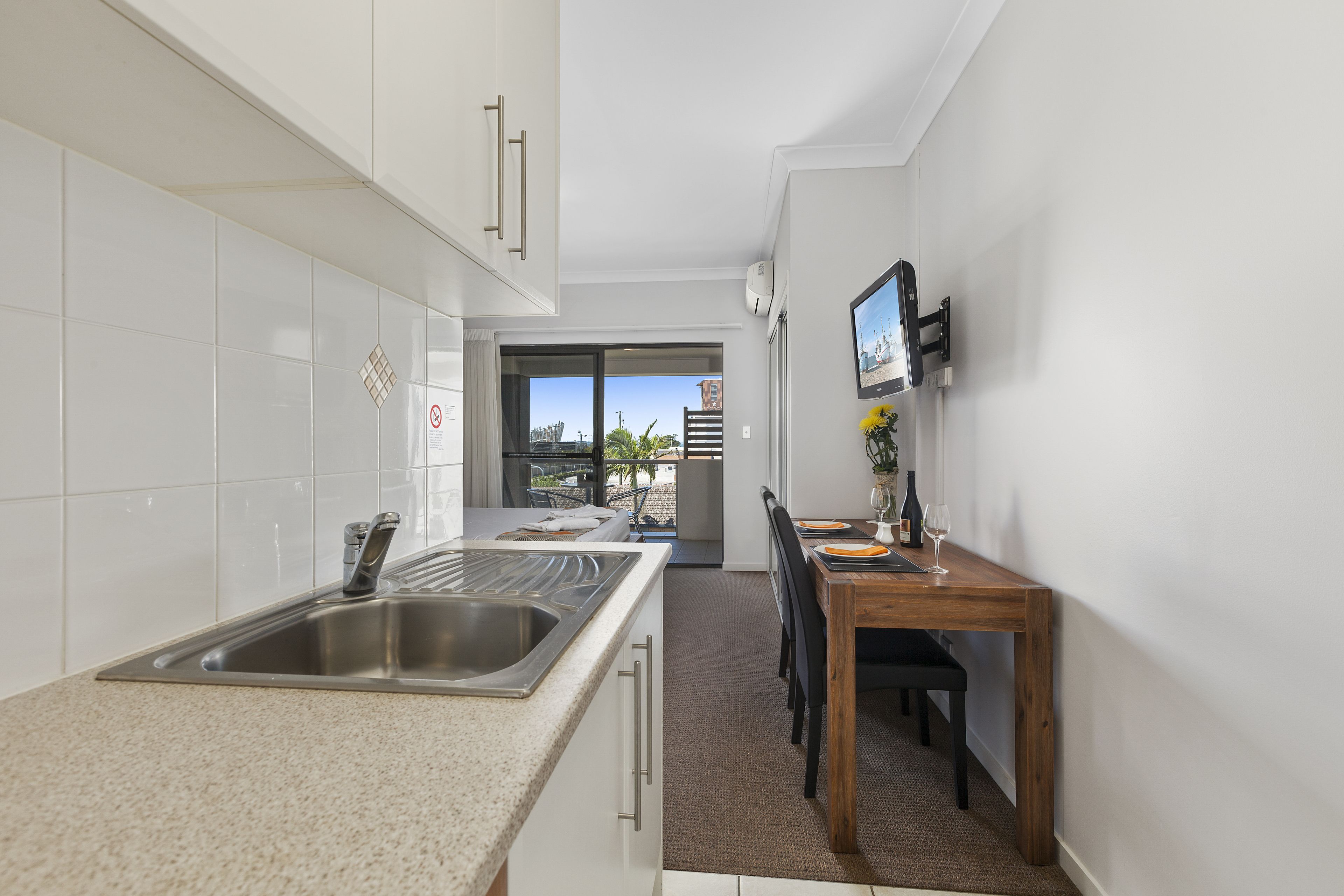 A modern kitchen with white cabinets, a stainless steel sink, and a wooden dining table with chairs.