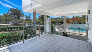 A spacious balcony with a clear view of a swimming pool and surrounding greenery. - La Vida on Anzac (Redcliffe)