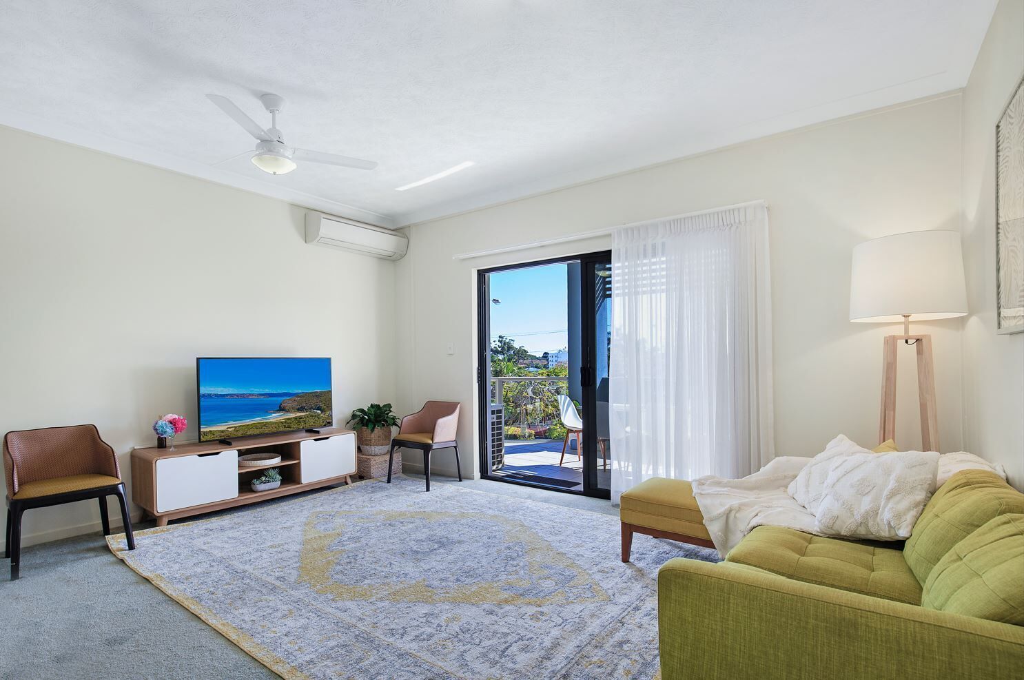 Ein Wohnzimmer mit Fernseher, Sofa, Sesseln und Blick ins Freie.