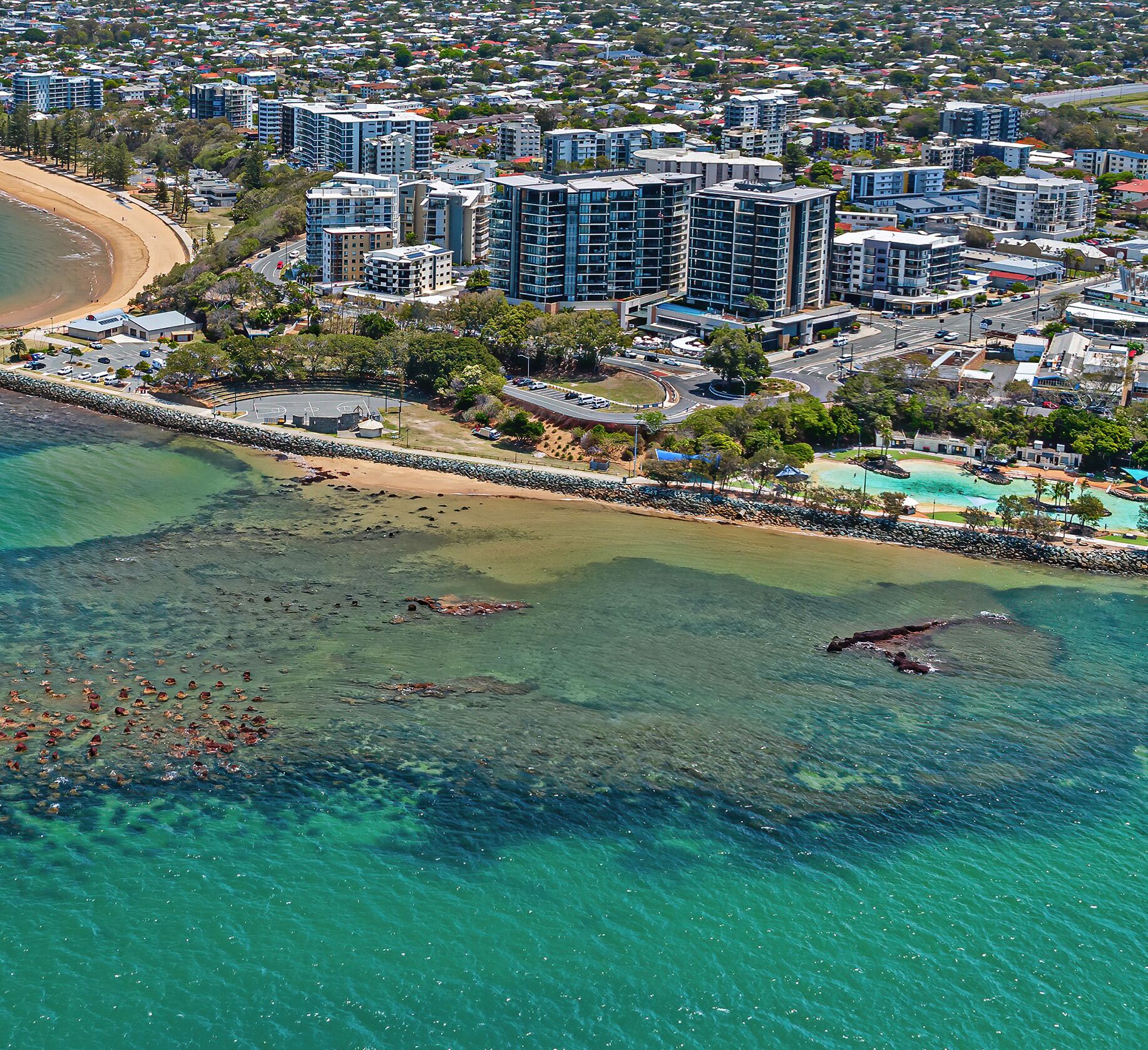 Vista aérea de una zona urbana costera con rascacielos, una playa y aguas turquesas cristalinas.