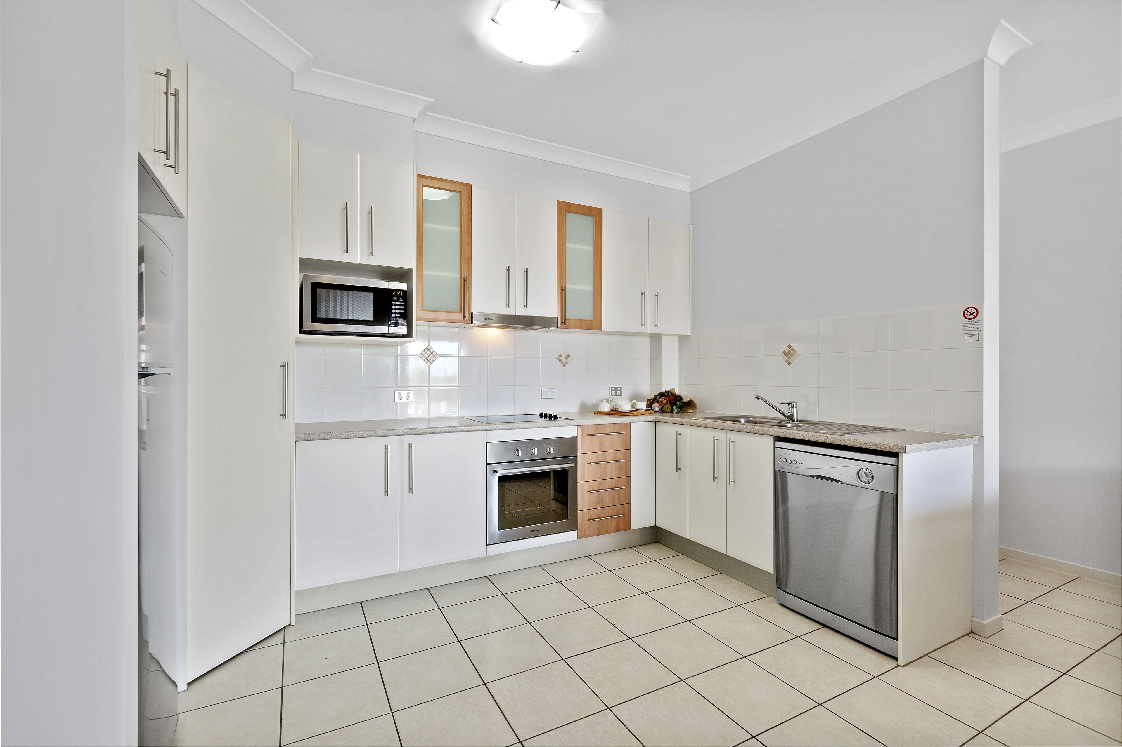 A modern kitchen with white cabinets, stainless steel appliances, and a tiled floor.