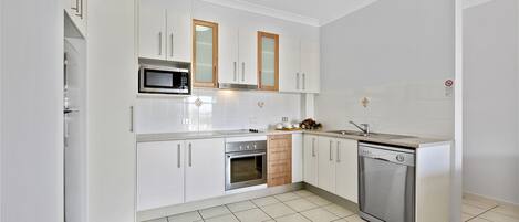 A modern kitchen with white cabinets, stainless steel appliances, and a tiled floor.