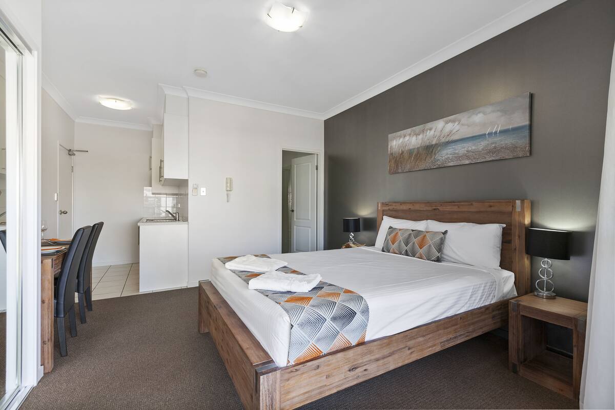 A modern bedroom with a wooden bed, a small desk, and a dining area.