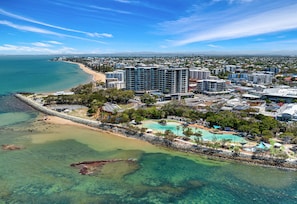 An aerial view of a coastal resort with high-rise buildings, a beach, and a clear blue sky. - La Vida on Anzac (Redcliffe)