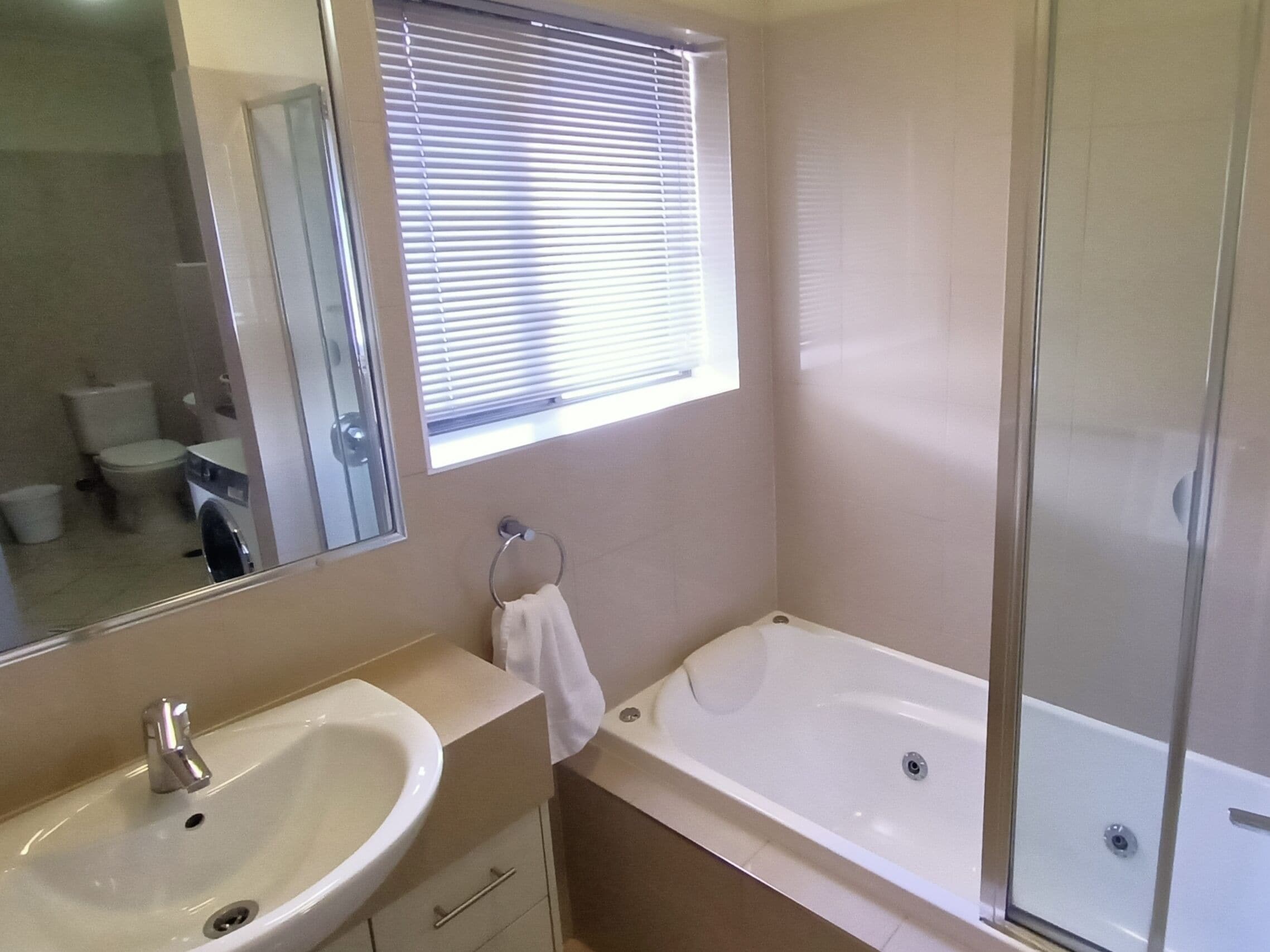 A bathroom with a sink, mirror, window, and shower.