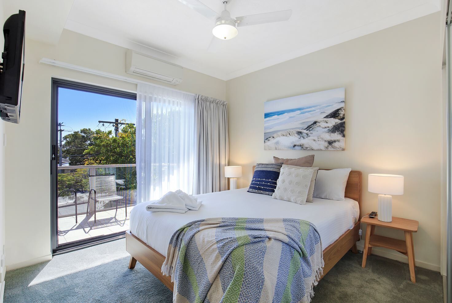A hotel room with a bed, a nightstand, a lamp, a painting, and a balcony with a view.