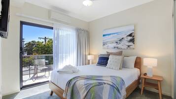 Quarto de hotel com cama, mesa de cabeceira, luminária, pintura e varanda com vista.