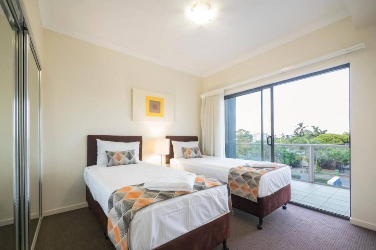 A hotel room with two beds, a large window, and a view of greenery outside.