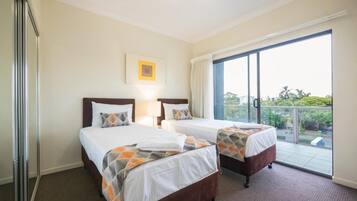 A hotel room with two beds, a large window, and a view of greenery outside.