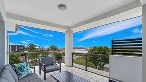 A balcony with a sofa, chairs, and a table, offering a view of the cityscape. - La Vida on Anzac (Redcliffe)
