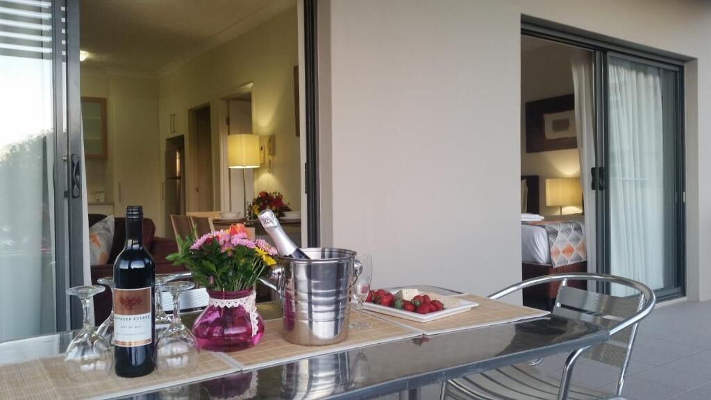 A glass table with a bottle, a metal bucket, and a vase with flowers.