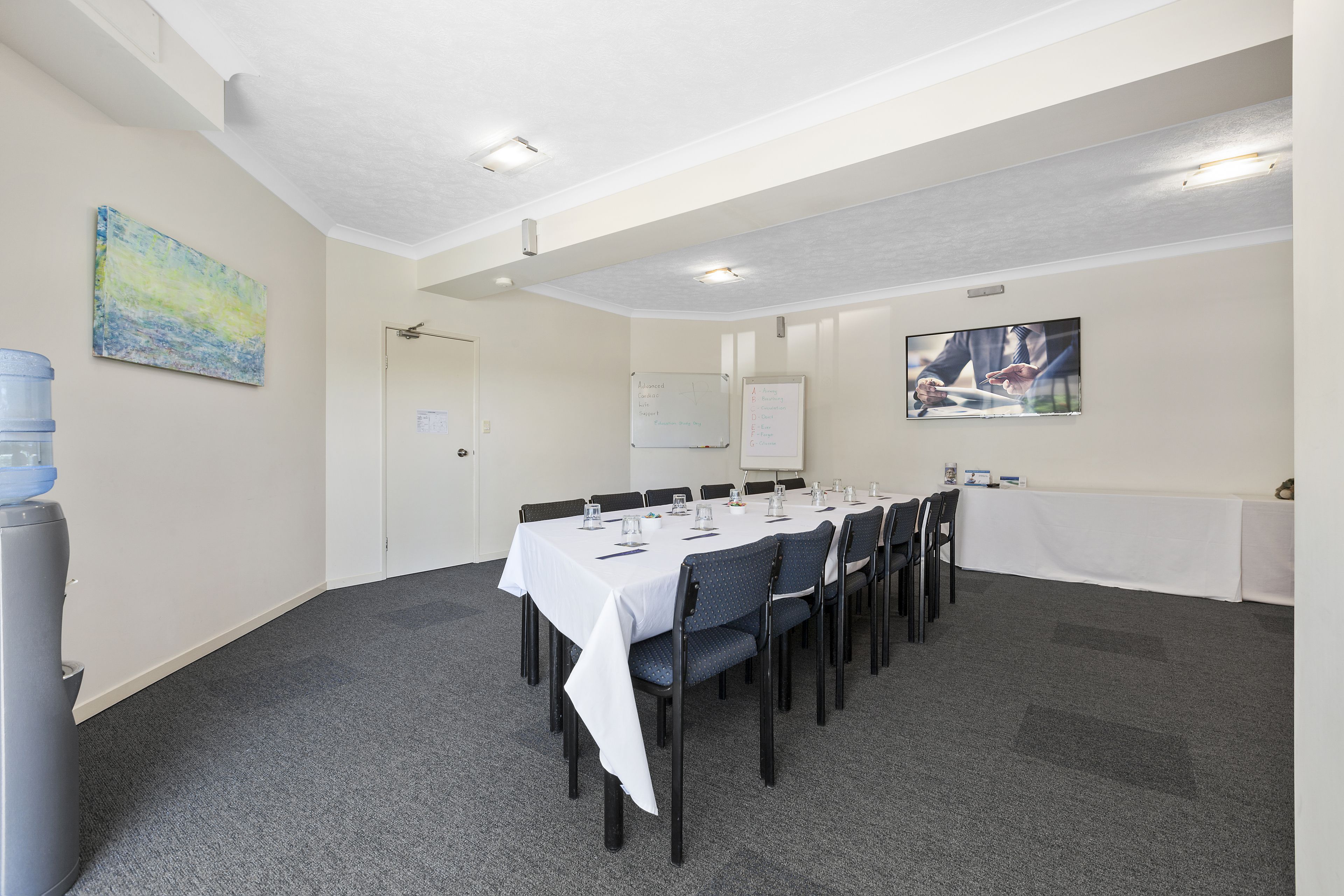 A conference room with a long table, chairs, a whiteboard, and a painting on the wall.