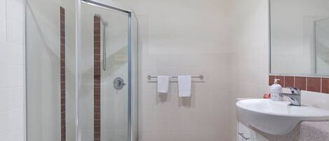 A bathroom with a glass-enclosed shower, white tiles, a sink with a mirror, and a towel rack.