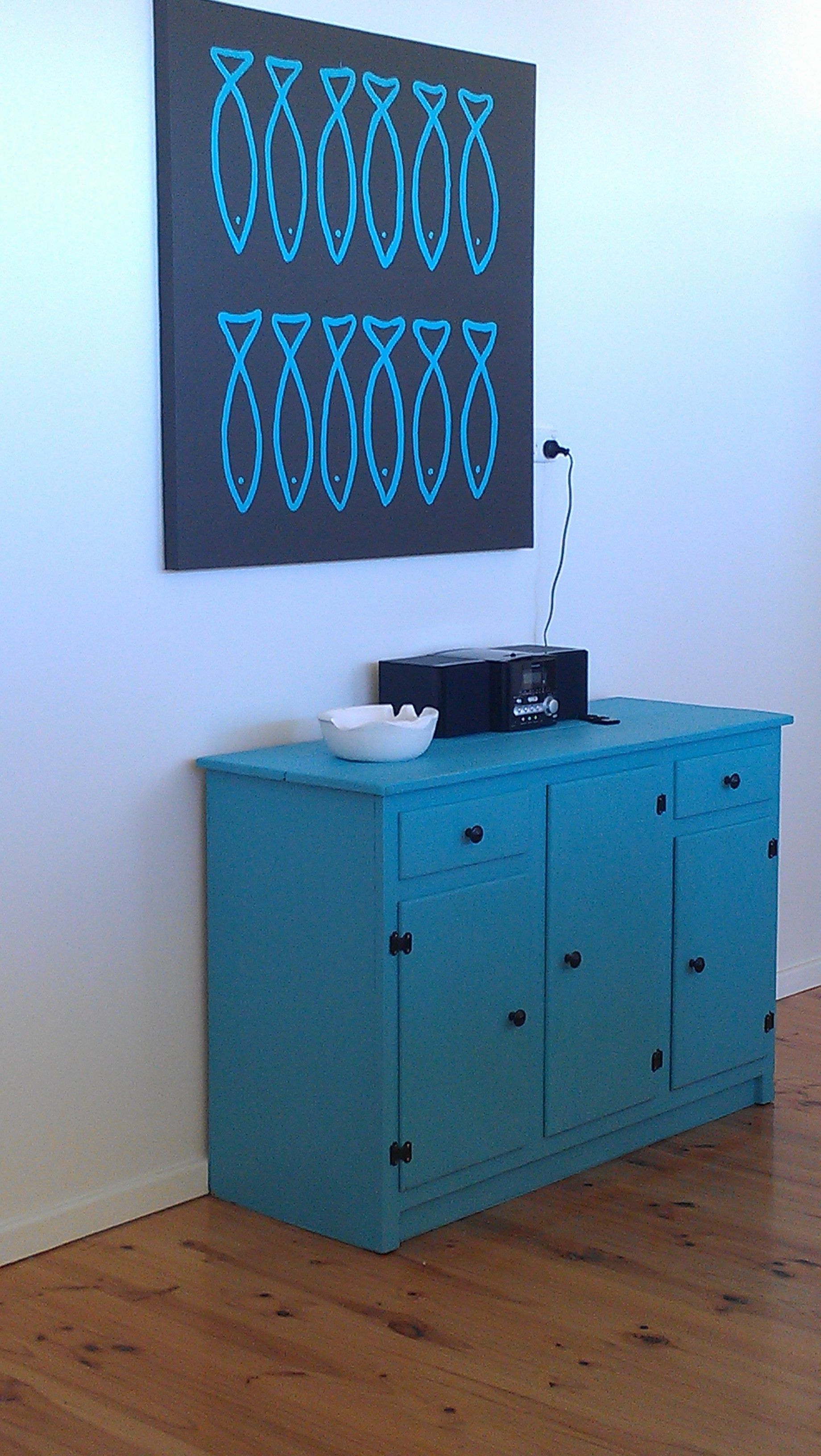Un mueble azul con una radio negra y un cuenco blanco encima.