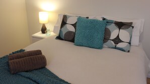 Un lit bien fait, avec une couverture bleue et deux serviettes marron, une lampe de chevet et des coussins à motifs.