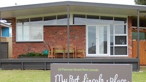 Une maison moderne dotée d’un grand porche, d’une façade en briques et d’une enseigne publicitaire pour un service de « chez-soi loin de chez soi ».