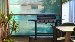 Une terrasse avec un barbecue, des chaises et une plante en pot.