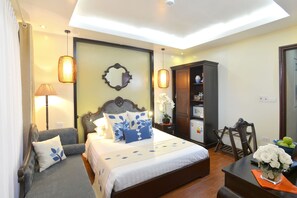 A hotel room with a bed, a sofa, a desk with a vase of flowers, a cabinet, and a mirror on the wall. - Finnegans Hotel (Hanoi)