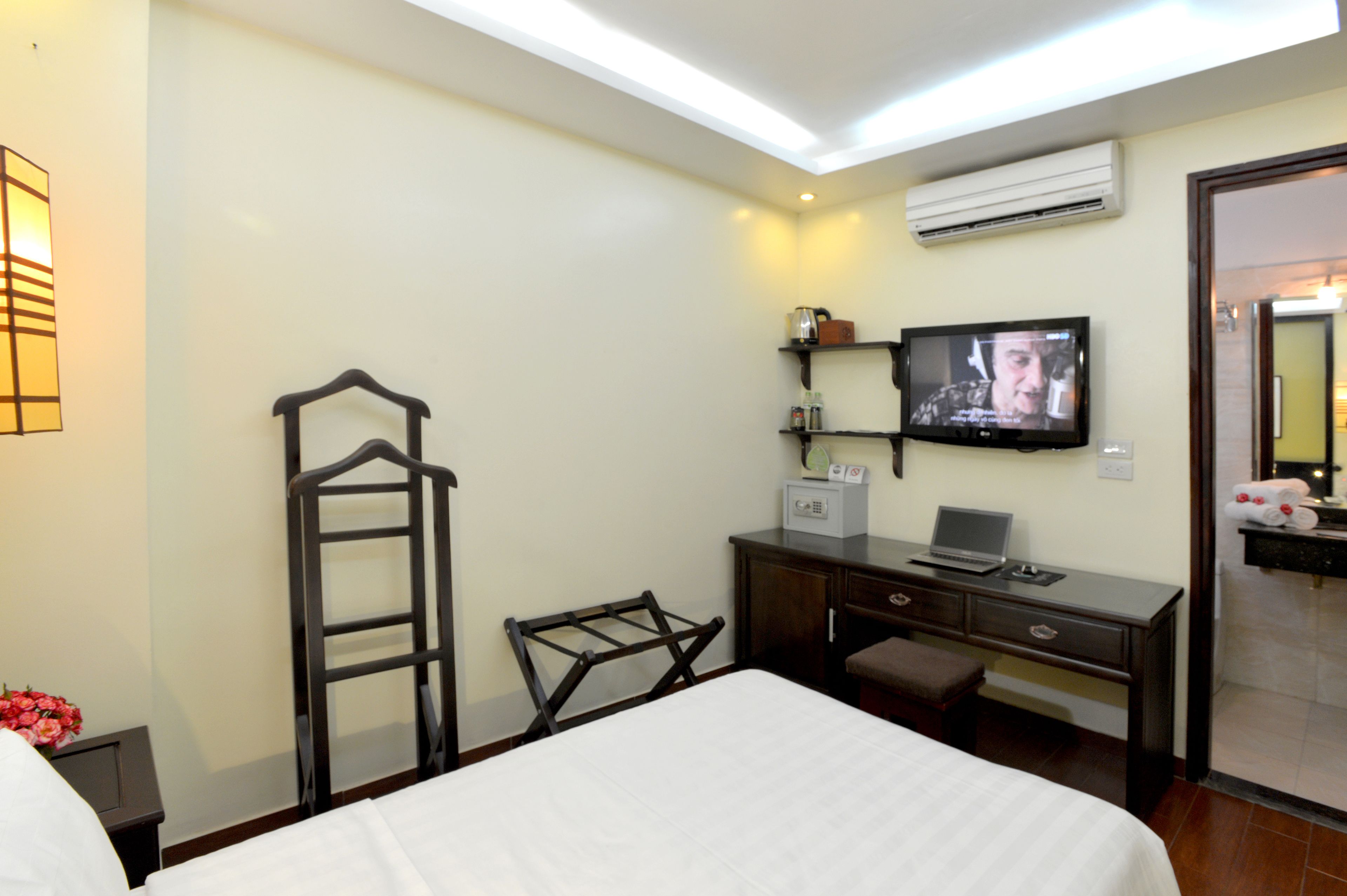 A hotel room with a bed, a desk with a laptop, a television, and a wardrobe.