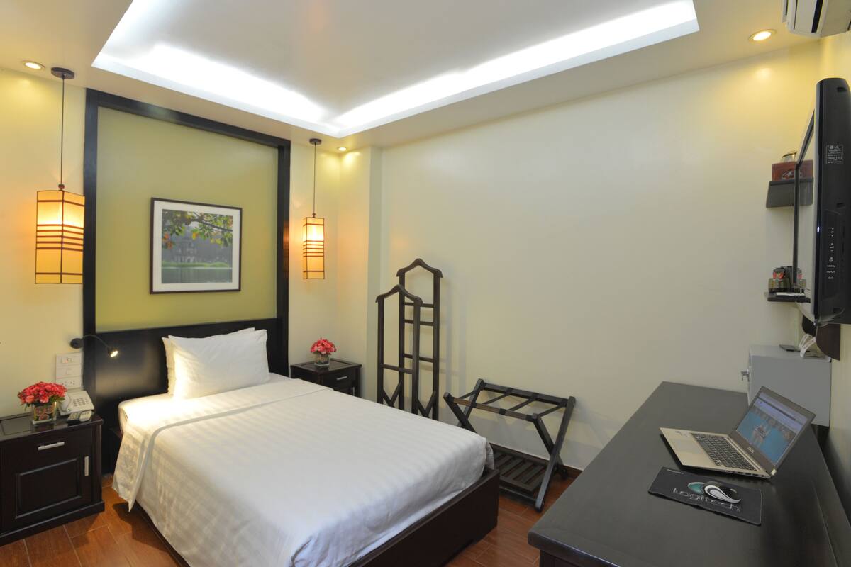 A hotel room with a bed, bedside tables, a desk with a laptop, and a TV.