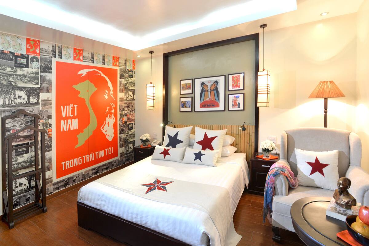 A hotel room with a bed, a chair, a nightstand, and a wall decorated with pictures and a large poster.