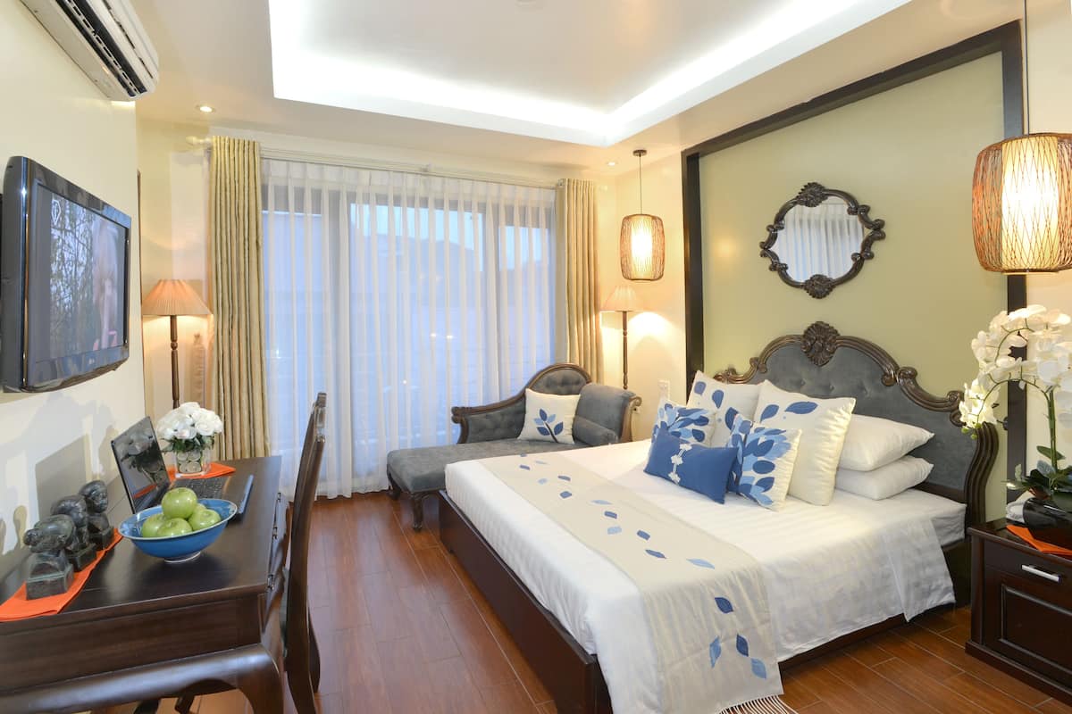 A hotel room with a bed, a desk with a laptop, a bowl of apples, and a lamp.