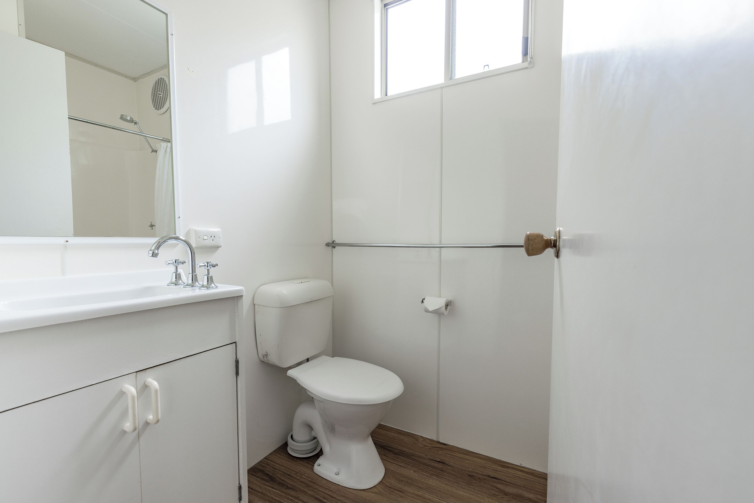 A bathroom with a white toilet, a sink with a mirror, and a window.
