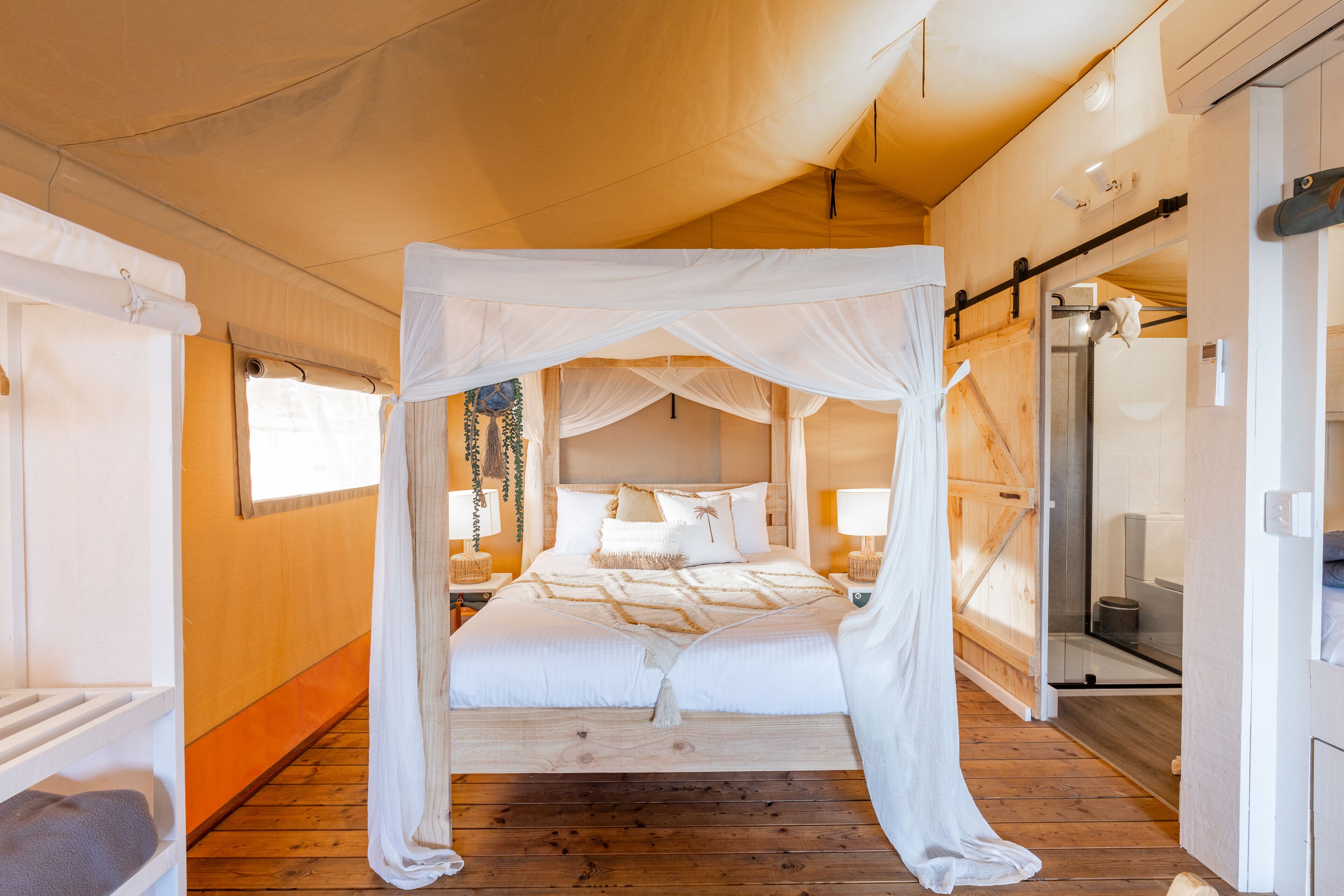 A spacious bedroom with a canopy bed, wooden flooring, and a walk-in shower.