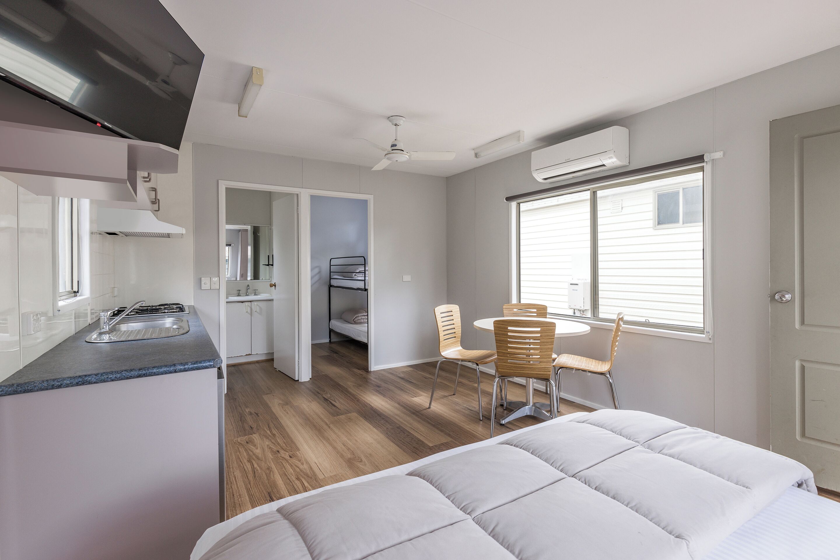 A modern kitchen with a built-in stove, a dining area with a table and chairs, and a bedroom with a large bed.