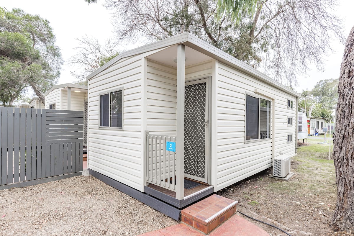 Une maison mobile de plain-pied, dotée d’un porche, d’une porte moustiquaire et d’un petit marchepied menant à l’entrée.