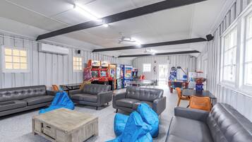 A spacious room with grey leather sofas, a wooden coffee table, and blue bean bags. There are arcade games and a ping pong table in the background.