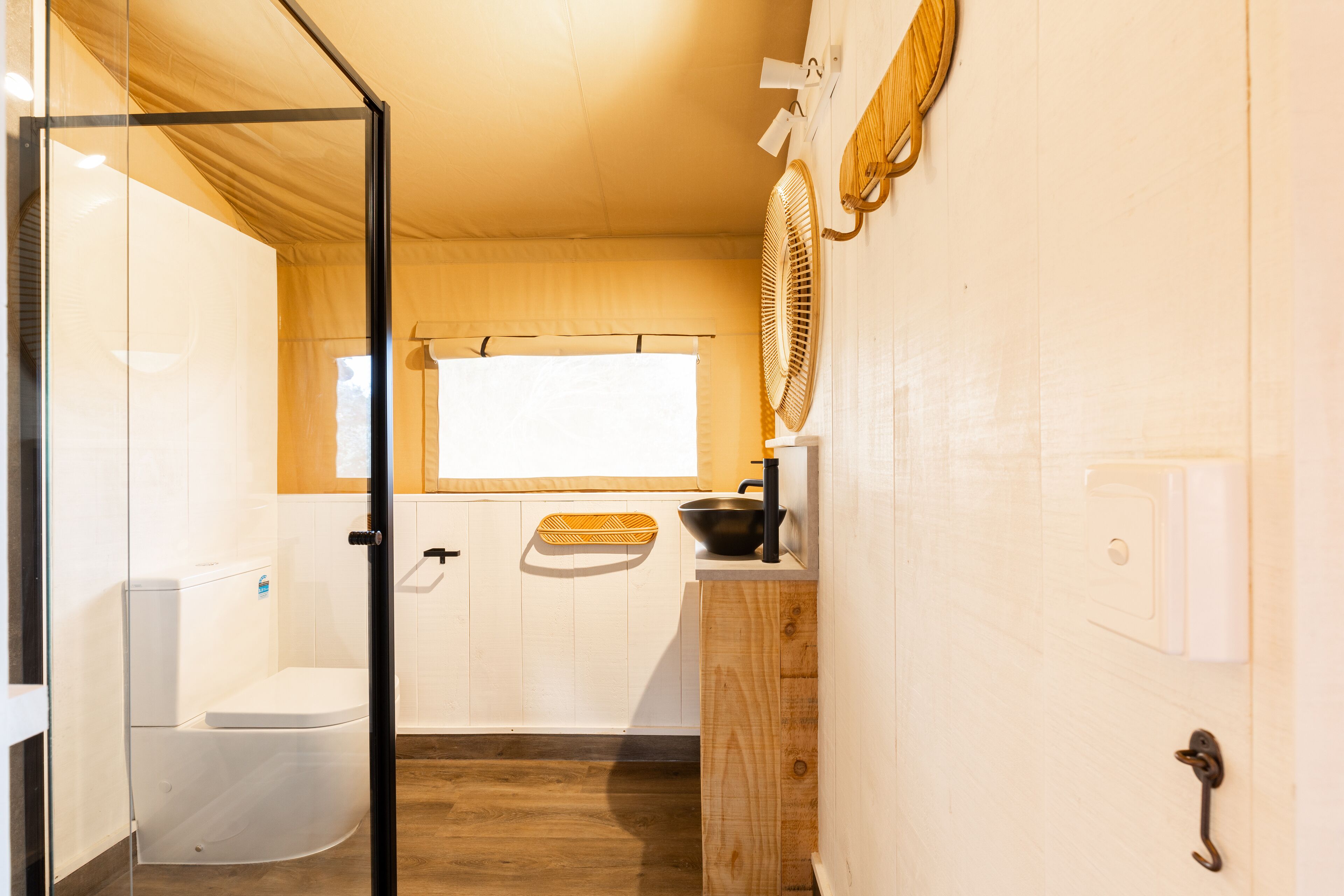 A compact bathroom with a glass shower enclosure, a white toilet, a wooden sink, and a window providing natural light.