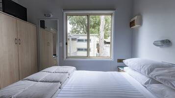 A bedroom with a large window, a bed, a wardrobe, and a bedside table.