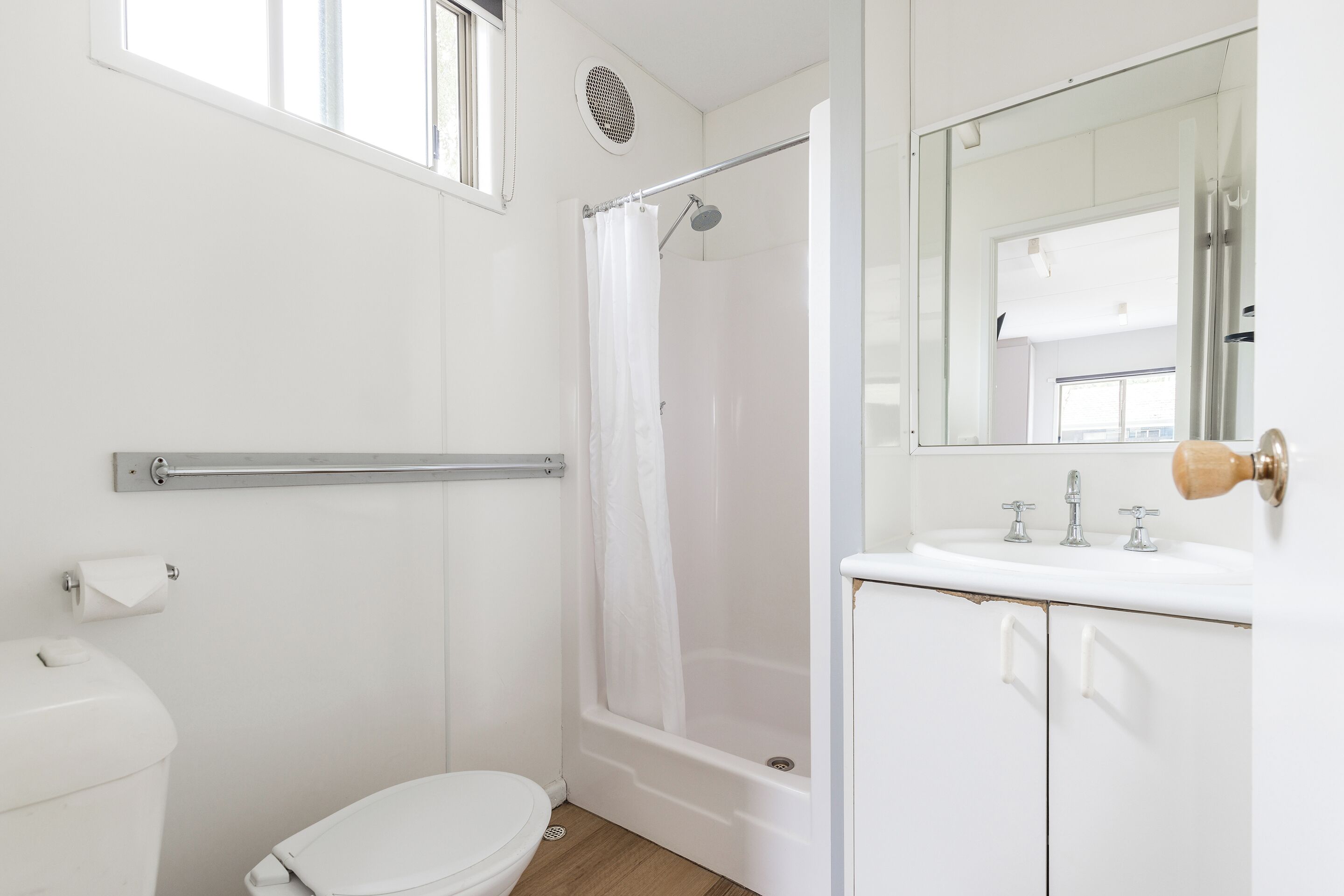 Ein Badezimmer mit Toilette, einer Duschkabine, einem Waschbecken und einem Spiegel sowie einem Fenster.