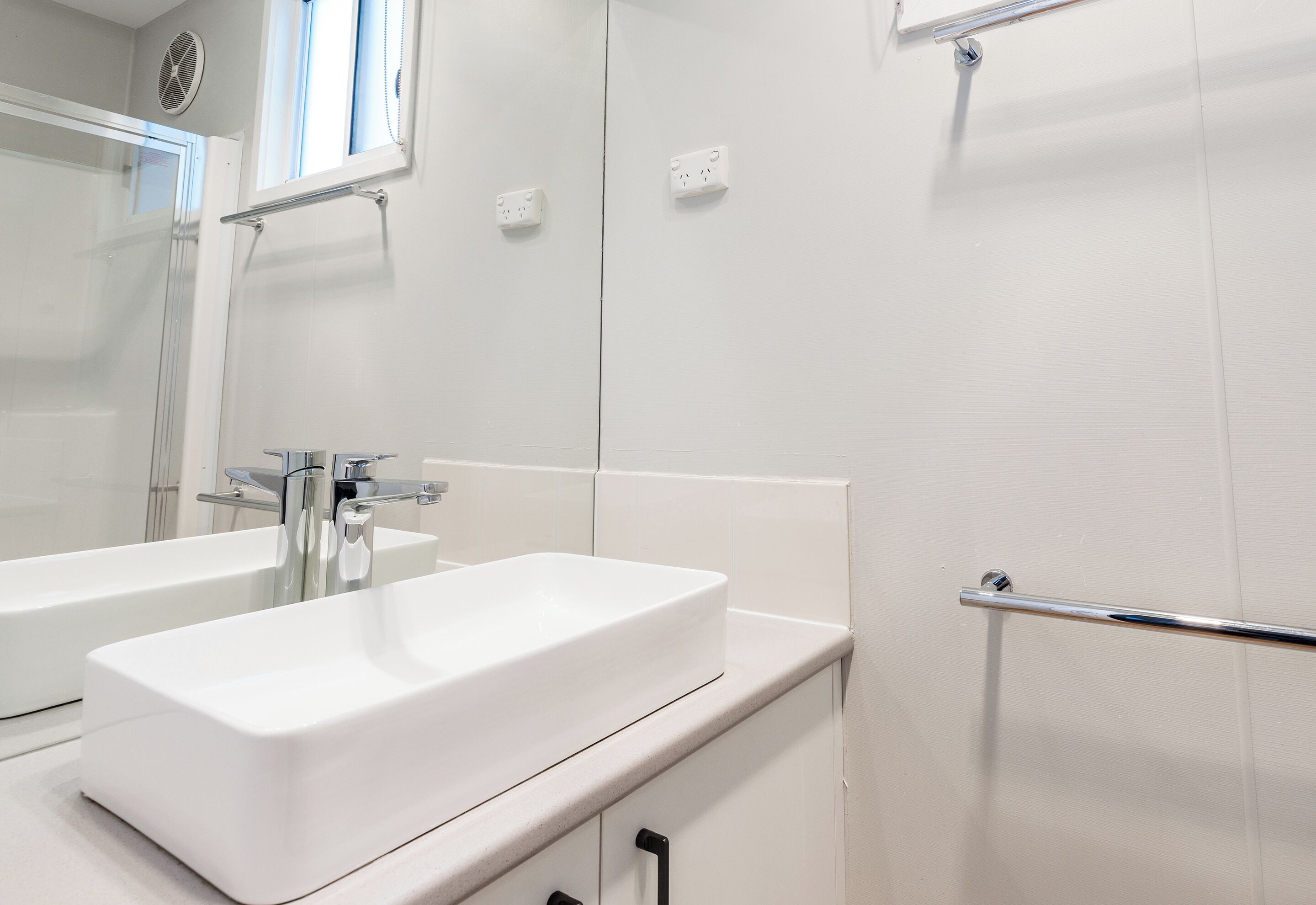Un baño moderno con dos lavamanos blancos, un espejo y una cabina de ducha de vidrio.