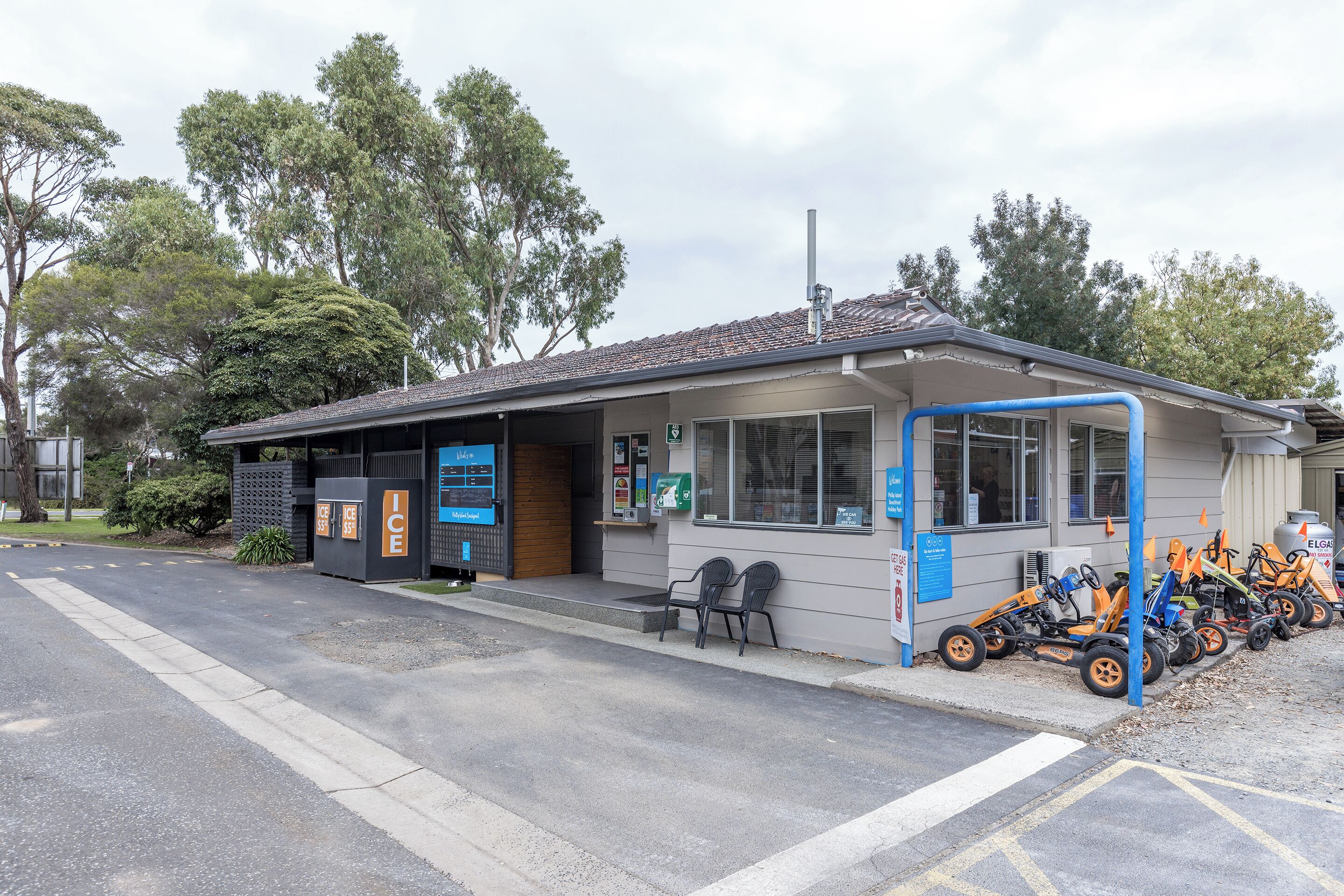 A small building with a covered area, a vending machine, and a row of orange go-karts parked outside.