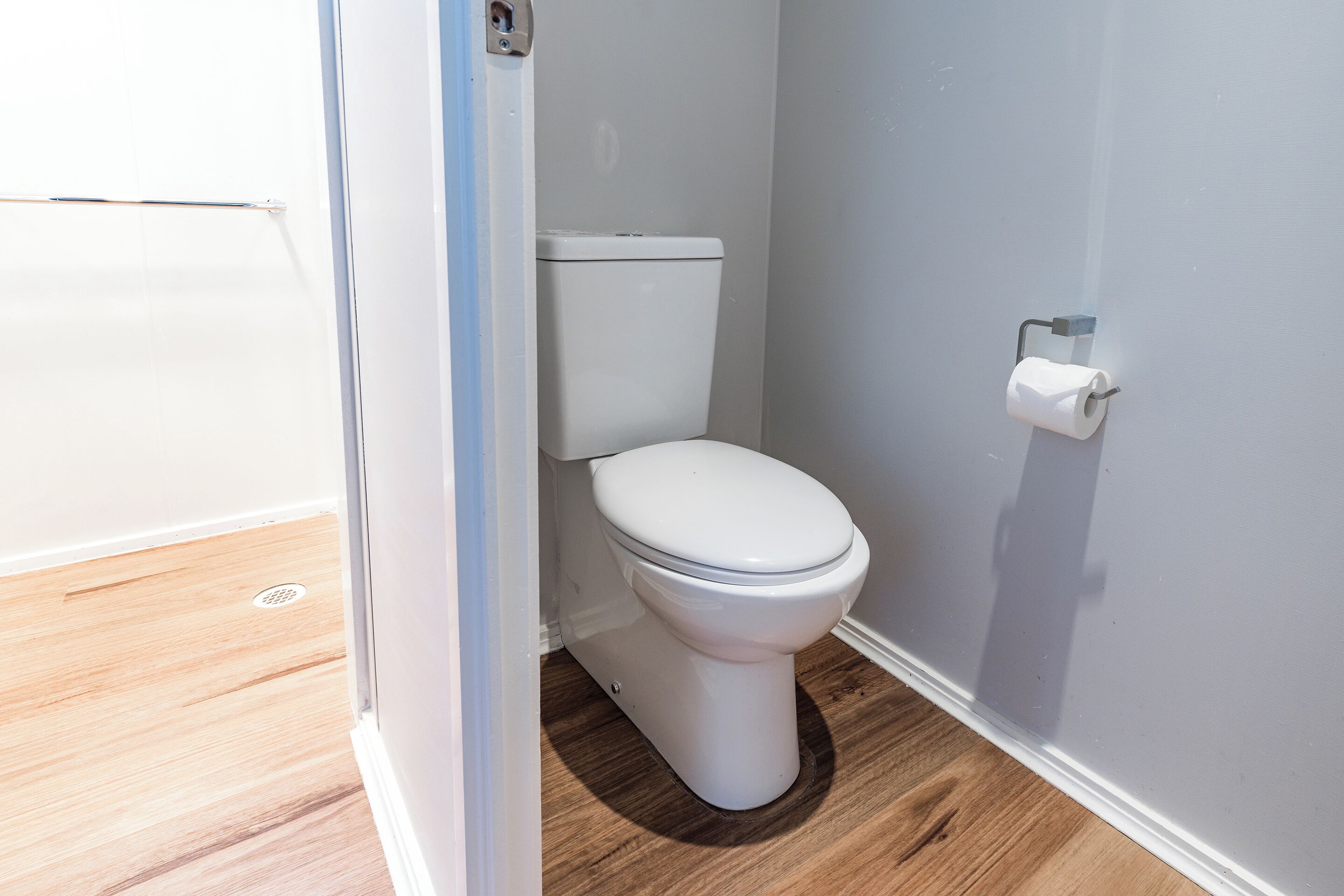 Un inodoro blanco en un baño con suelo de madera y pared blanca.