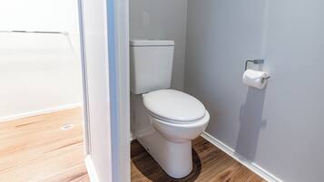 Un inodoro blanco en un baño con suelo de madera y pared blanca.
