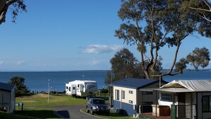 A caravan park with a road, a car, and a boat trailer. - NRMA Phillip Island Beachfront Holiday Park (Cowes)