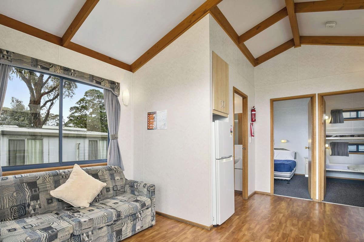 Une pièce avec un canapé à motifs, une fenêtre avec des rideaux, un plafond en bois et une porte donnant sur un espace avec des lits superposés.